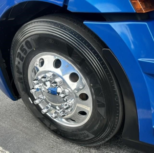 Truck wheel of a blue Freightliner Cascadia showing chrome hubcap and tire with visible branding.
