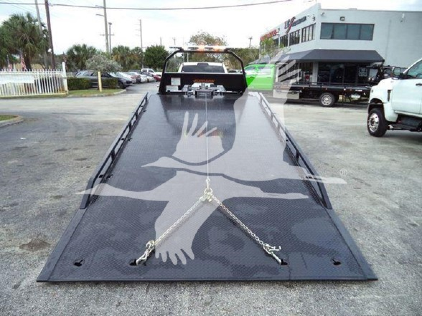 Flatbed tow truck rollback bed with securing chains and D-rings, viewed from front perspective.