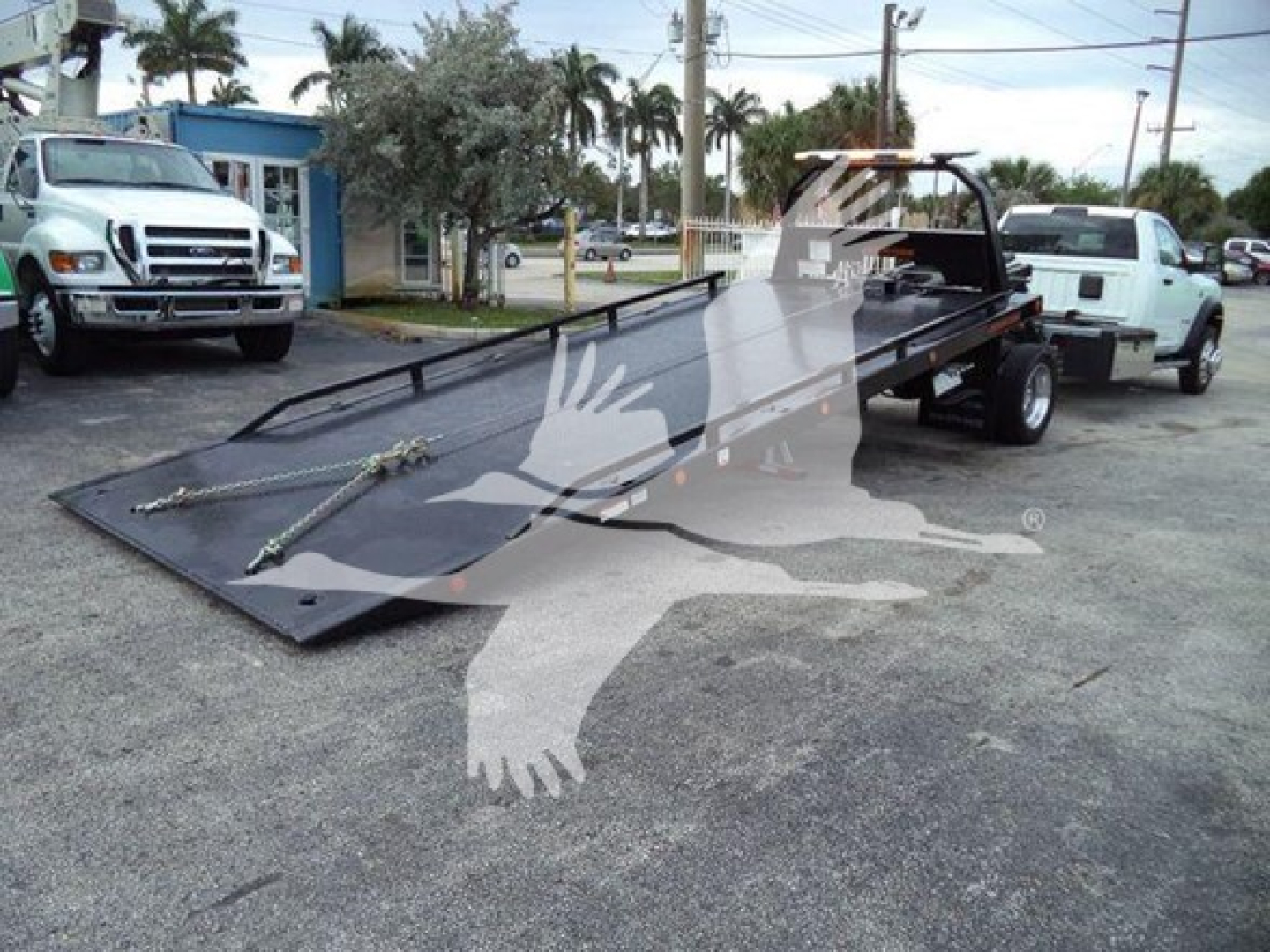 Ram 5500 rollback tow truck flatbed with two trucks in background, VIN plate and equipment bed visible.