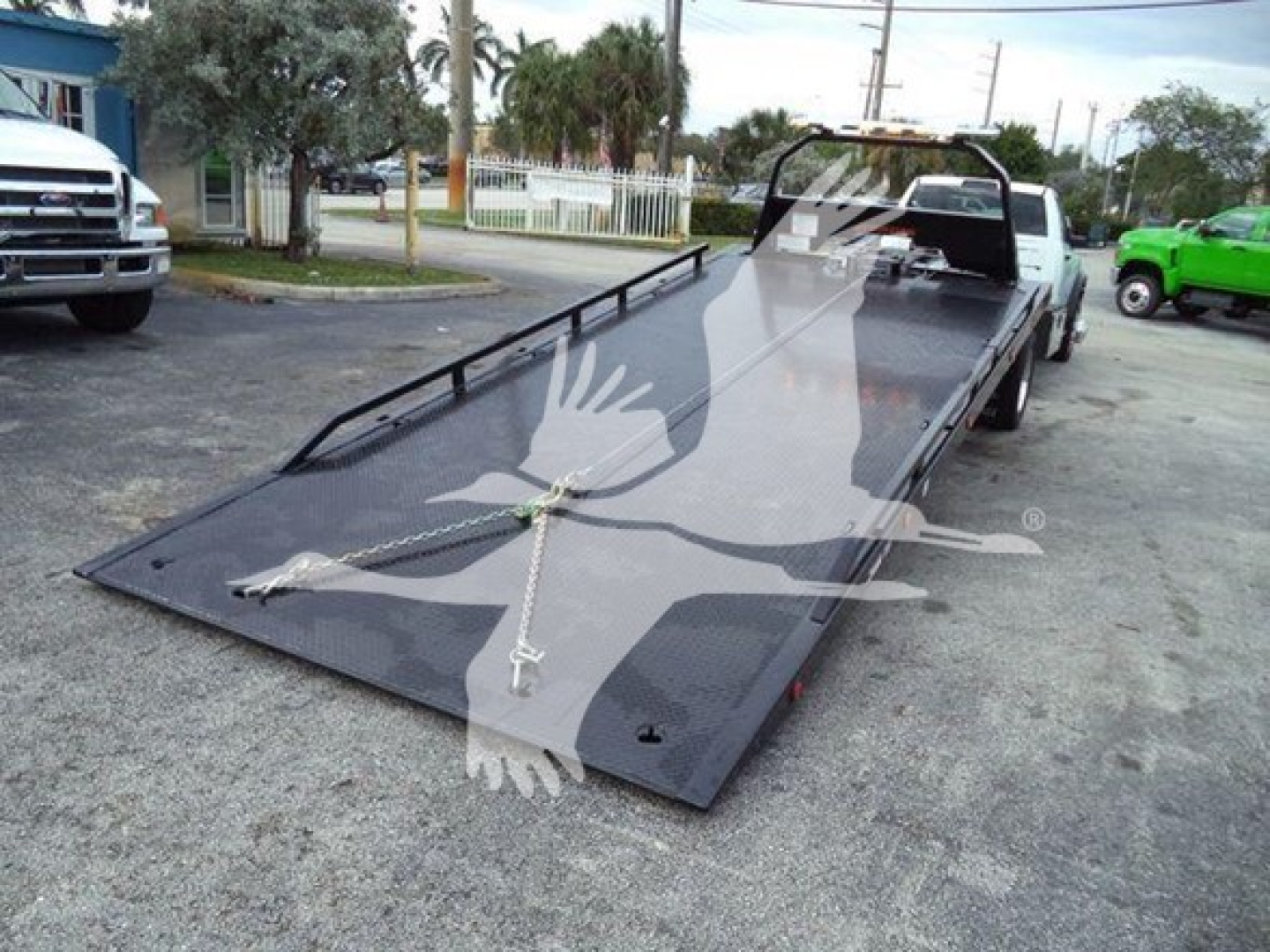 Ram 5500 rollback truck bed with a lowered steel ramp platform and a winch tie-down; visible text not legible; part of a towing vehicle.