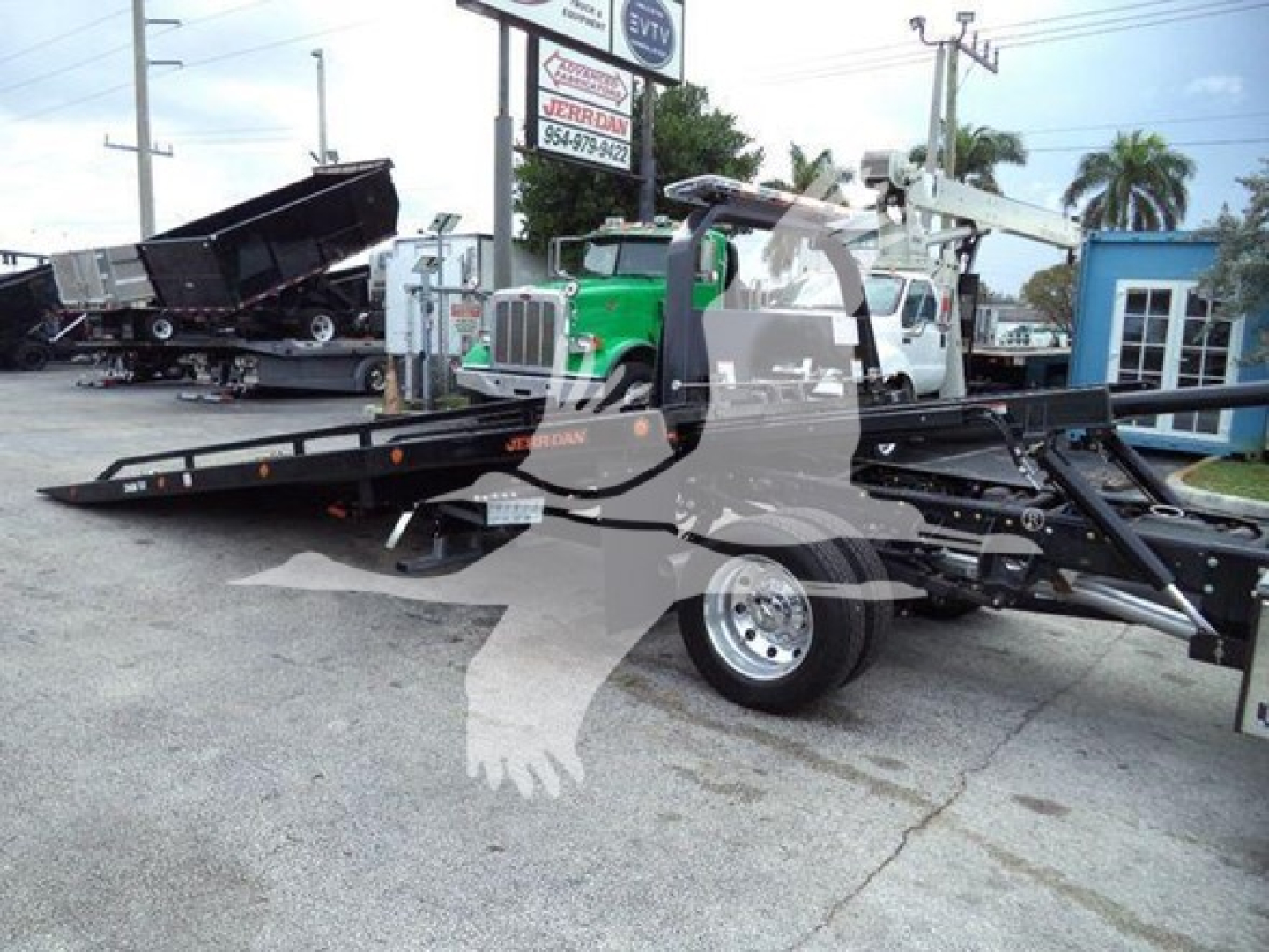 Truck with rollback equipment showing long flatbed and wheel with Ramp/haul setup; faint lettering on equipment includes 'Jerr-Dan' branding and a green truck in background.