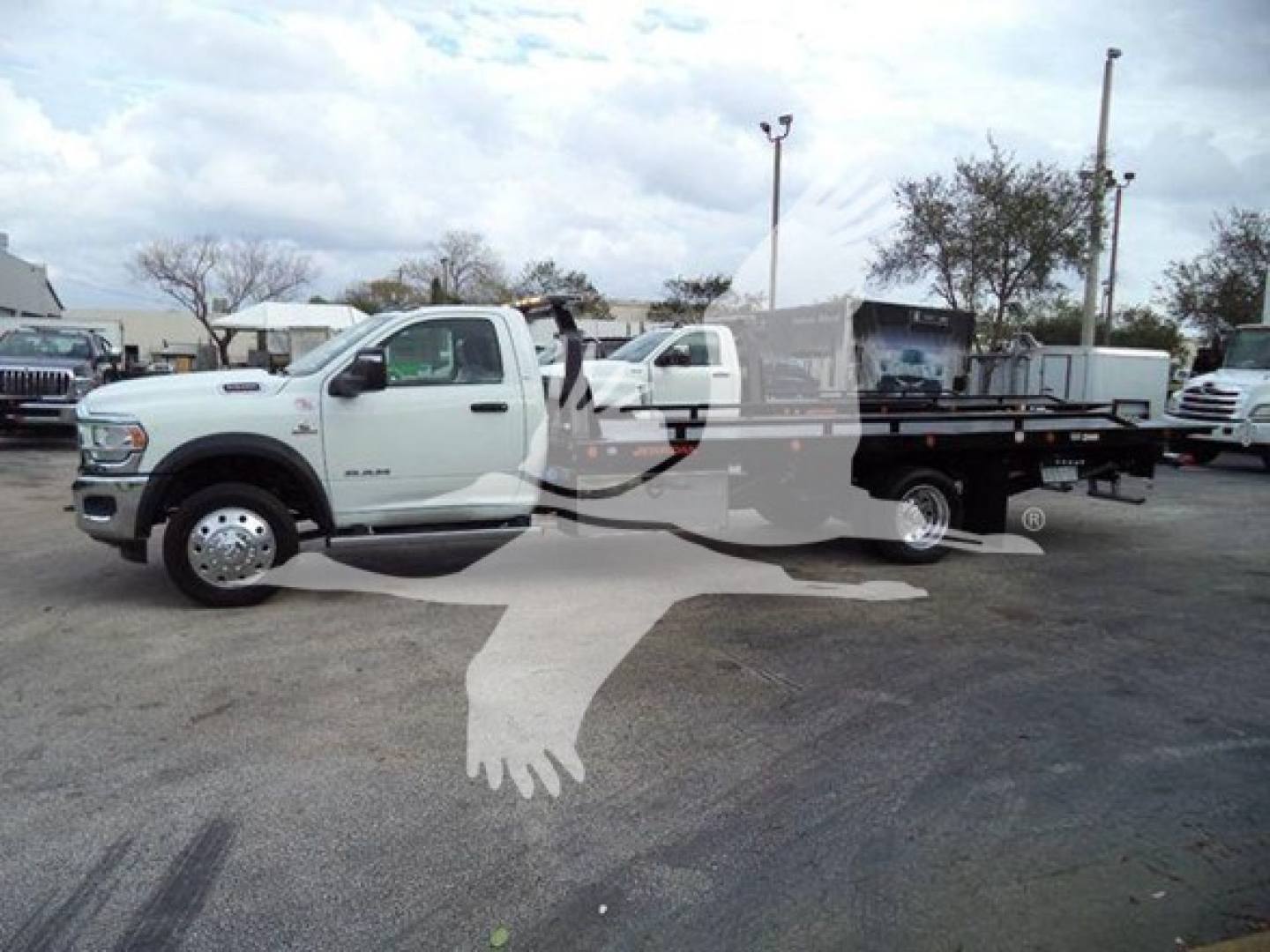Ram 5500 SRW flatbed rollback truck in a dealership lot, white cab with long flatbed and tow equipment visible.