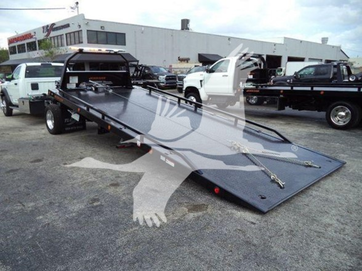 Flatbed tow truck bed on a new Ram 5500 SLT with a long tilt/rollback bed in a dealership lot.