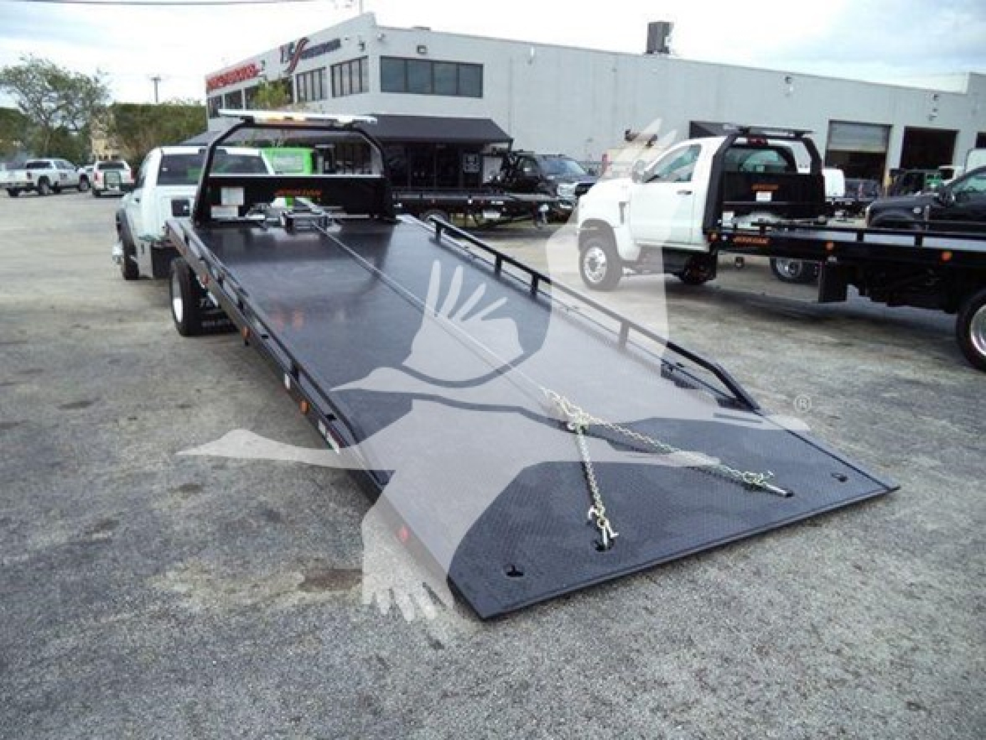 Ram 5500 SLT rollback tow truck with a long black flatbed and ramps, viewed from front-left side in a dealership lot.