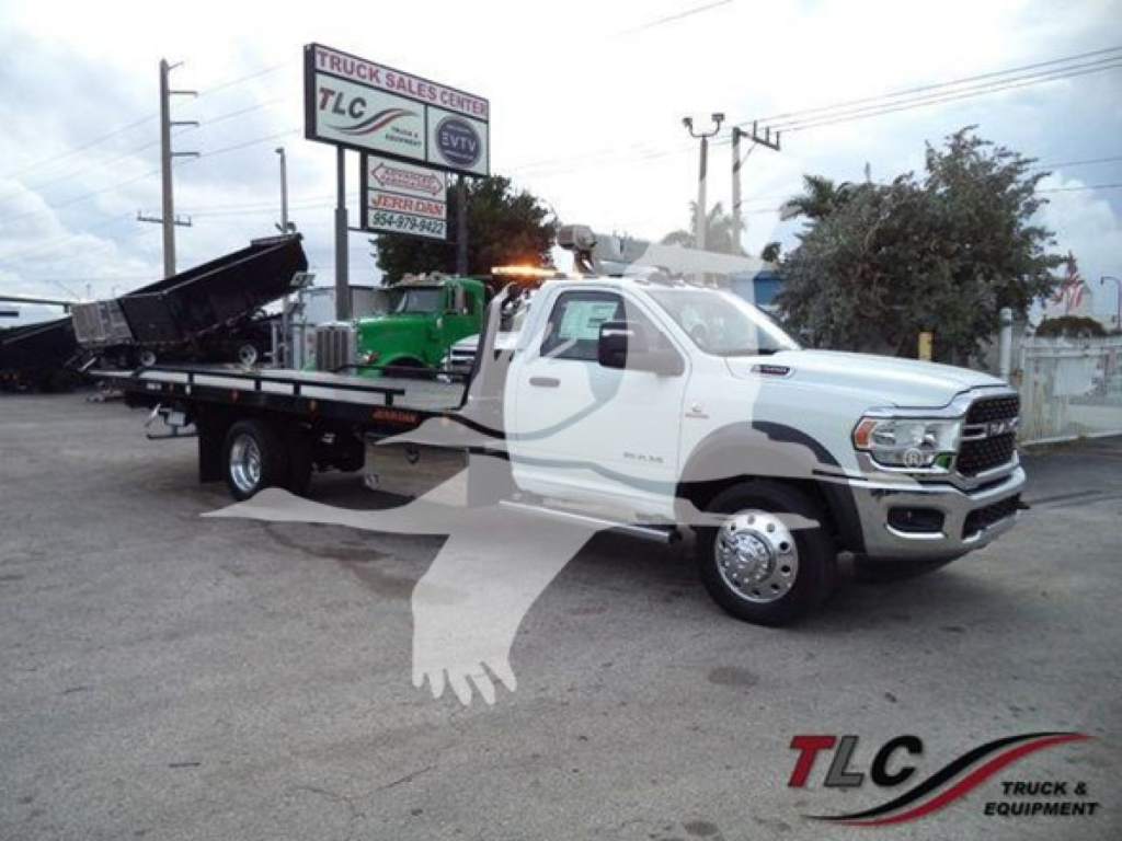 Ram 5500 tow truck in pickup bed rollback configuration showing white cab and flatbed, TLC Truck Sales Center signage in background.