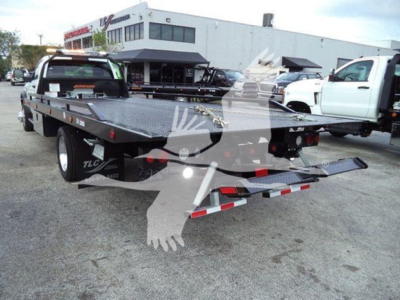 Flatbed tow truck with a 2024 Ram 5500 SLT, rollback bed, in a dealership lot showing rear and side view.