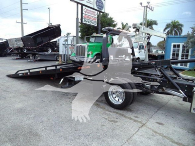 Truck with rollback equipment showing long flatbed and wheel with Ramp/haul setup; faint lettering on equipment includes 'Jerr-Dan' branding and a green truck in background.