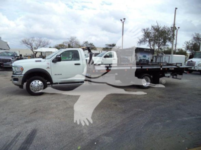 Ram 5500 SRW flatbed rollback truck in a dealership lot, white cab with long flatbed and tow equipment visible.