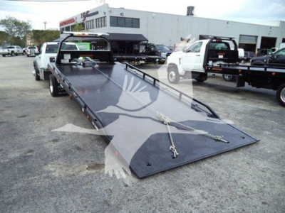 Ram 5500 SLT rollback tow truck with a long black flatbed and ramps, viewed from front-left side in a dealership lot.