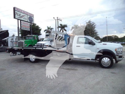 Ram 5500 rollback tow truck in a dealership lot, white cab, long flatbed with hydraulic system visible.