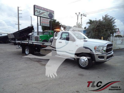 Ram 5500 tow truck in pickup bed rollback configuration showing white cab and flatbed, TLC Truck Sales Center signage in background.