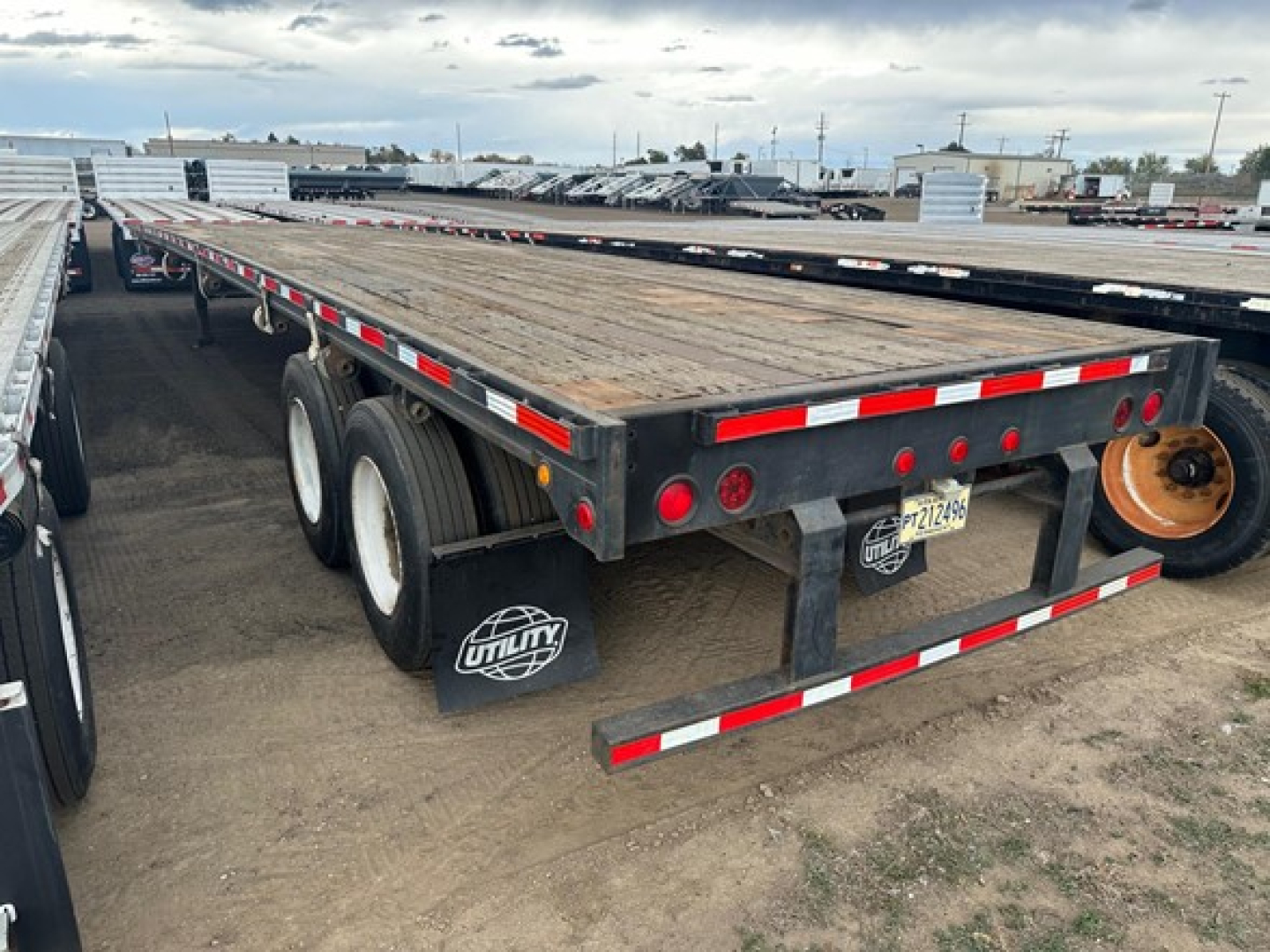 Flatbed trailer (Fontaine Velocity) showing dual rear axles and wooden deck, with red/white reflective tape along edges; trailer fenders, mud flaps, and spare wheel mounted at rear. Visible license plate area and light bar.