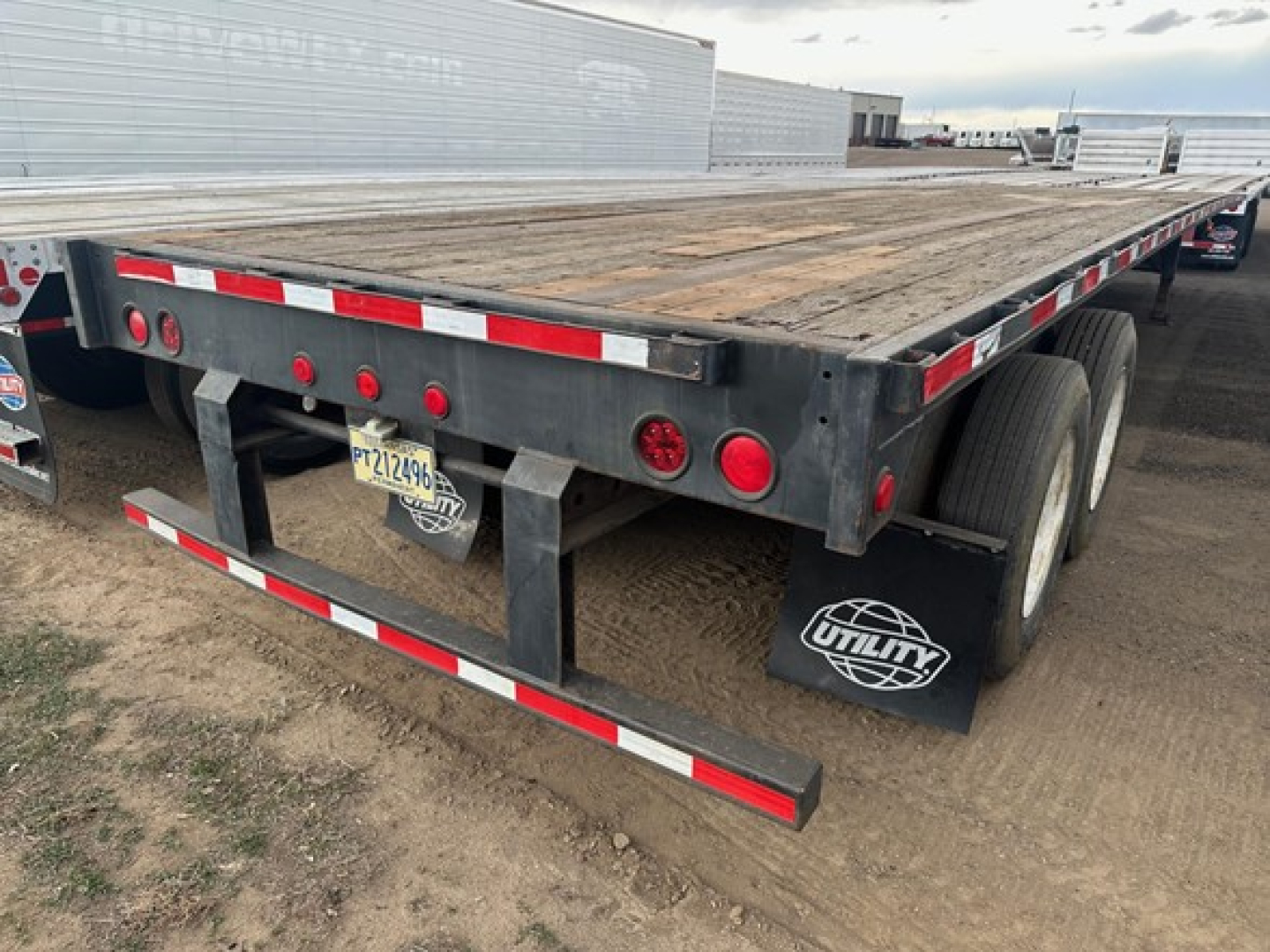 Flatbed trailer rear view showing wooden deck, dual rear axles, and Utility mudflap. License plate and red taillights visible.