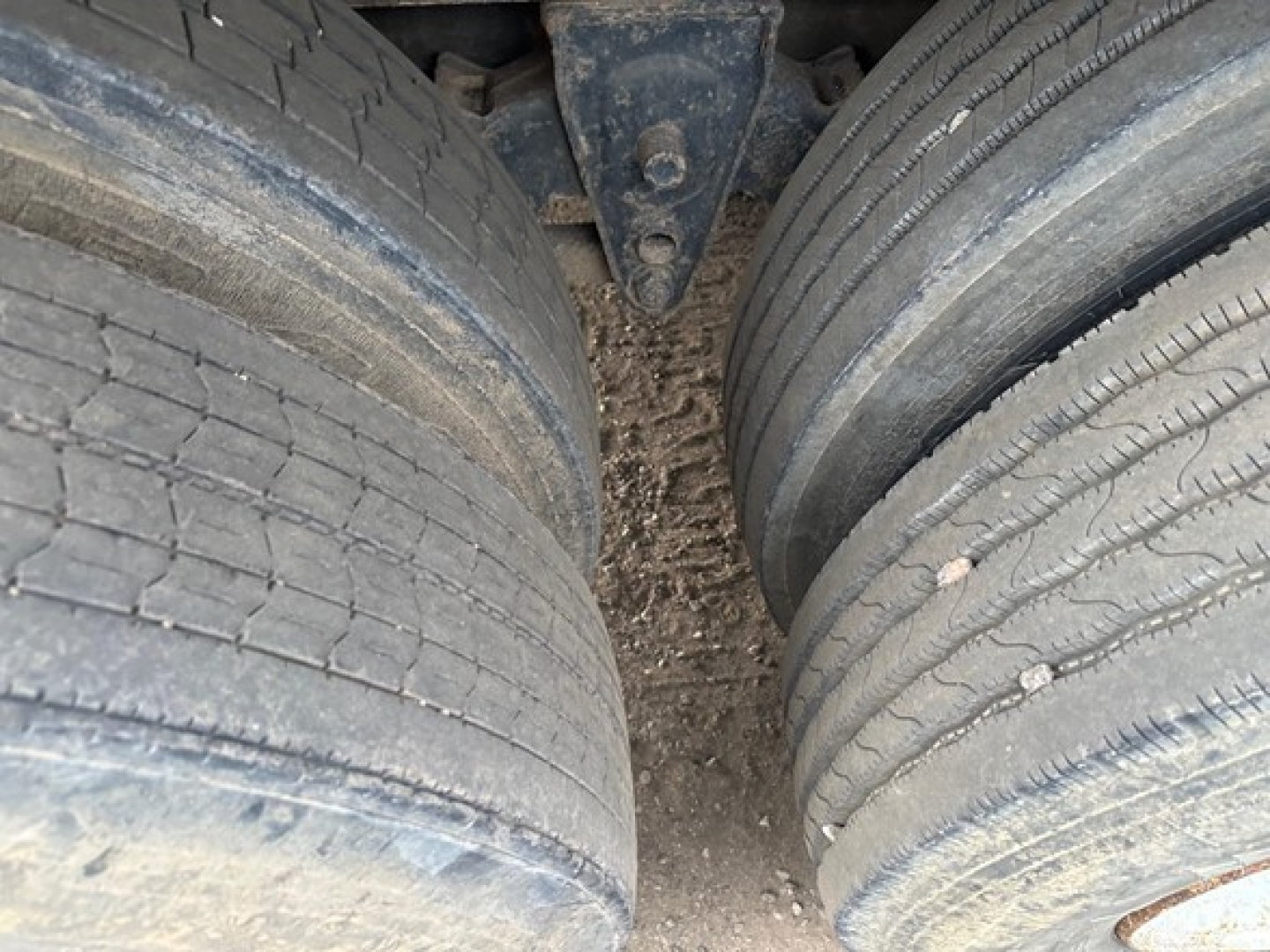 Dual rear trailer tires with tread detail and dirty ground between them; view shows back of chassis components between tires.