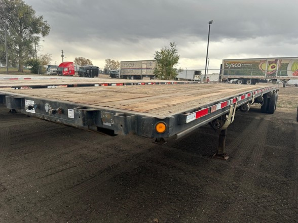 Flatbed trailer with wooden deck showing rear corner and wheels, Fontaine Velocity listing.