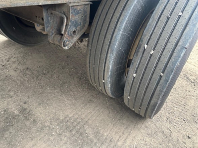 Flatbed trailer wheel area showing dual rear tires and undercarriage components.