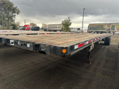 Flatbed trailer in a yard showing wooden deck and rear light assemblies.
