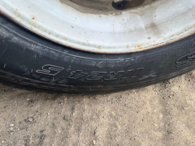 Flatbed trailer wheel and tire close-up showing tire sidewall text and wheel rim.