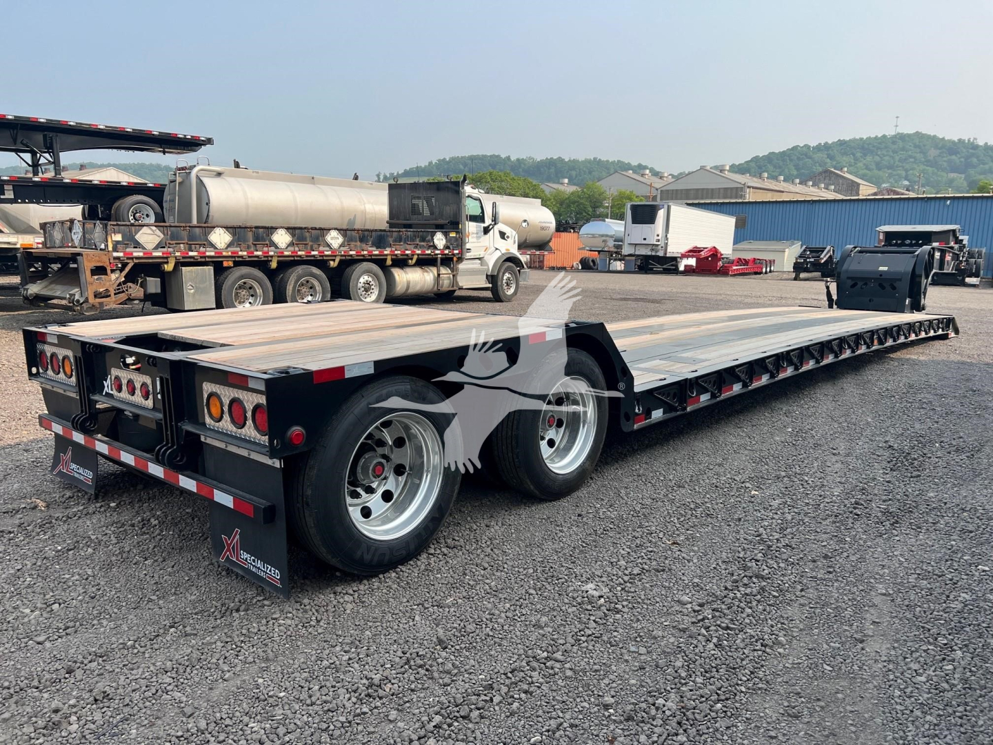 Flatbed trailer in a used trailers yard, XL Specialized XL80HDE plate and dual rear axles, metal deck, rear lights, and wheel fenders visible.