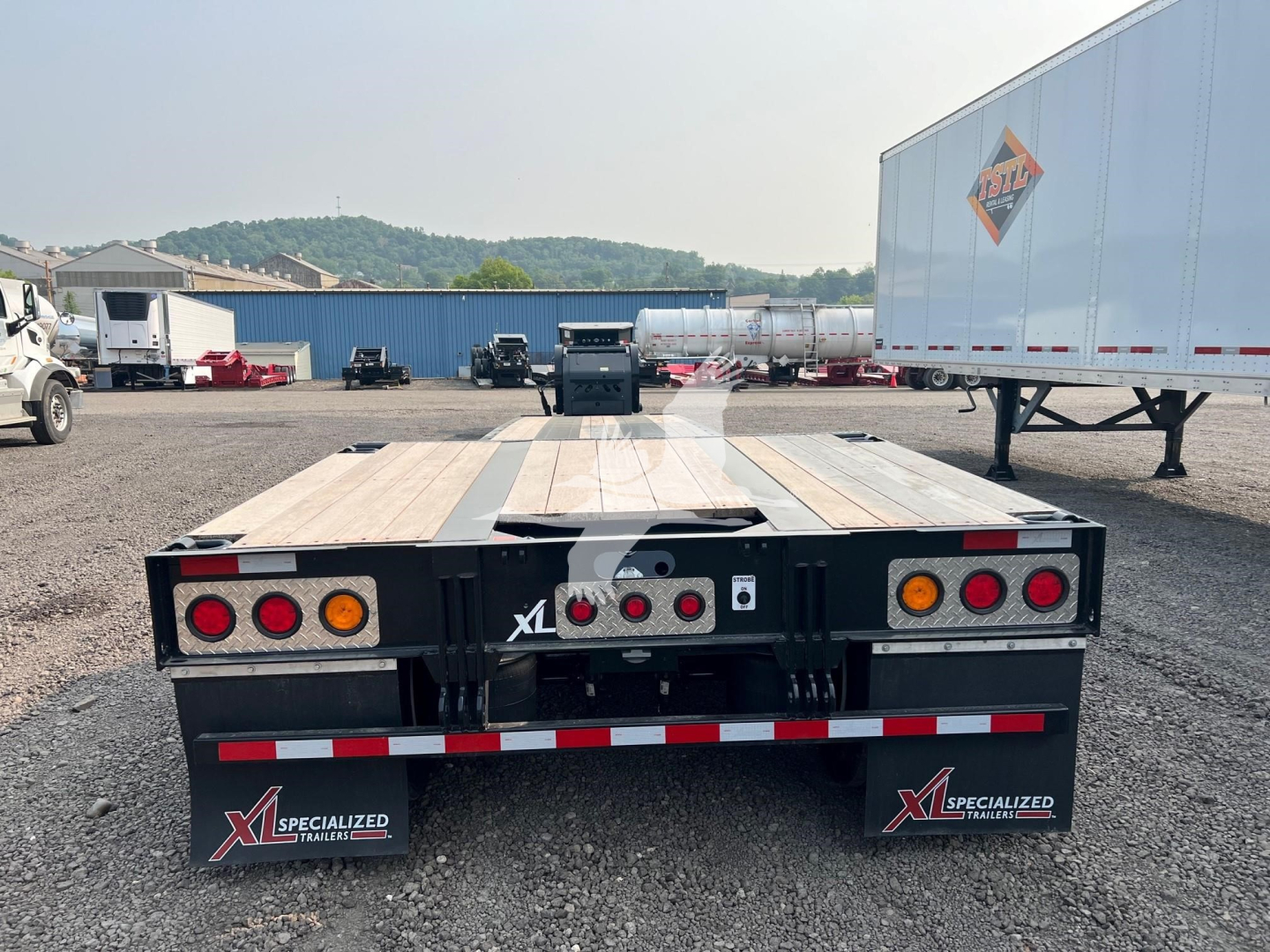 Lowboy trailer rear view showing wooden deck, taillights, and mud flaps with XL Specialized branding.