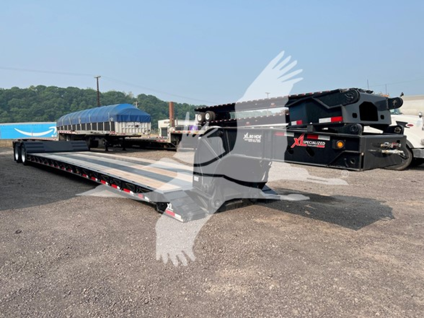 Lowboy trailer in yard showing XL Specialized XL80HD E80 base with hydraulic gooseneck and long flat deck, side rails, and blue tarped load in background.