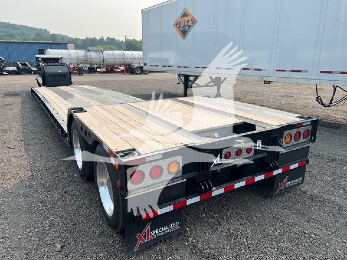Trailer deck of a lowboy trailer showing rear view with lights and reflective tape, Specialized XL branding on mudflaps and wheel wells.