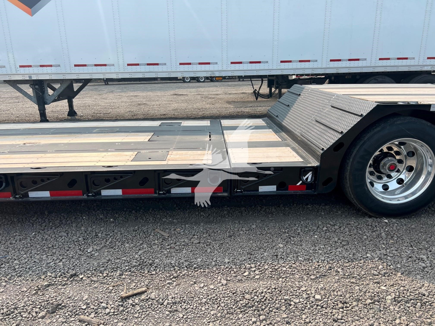 Trailer side view showing lowboy deck with metal surface and rear wheel, plus reflective tape; no legible model text visible.