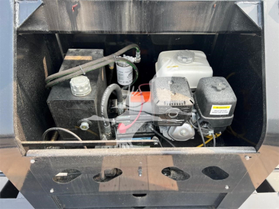 Trailer engine bay showing compact 4-stroke engine with white coolant reservoir, black hydraulic tank, and wiring in a lowboy trailer compartment.