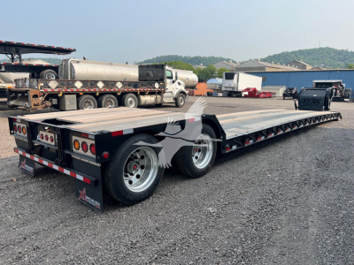 Flatbed trailer in a used trailers yard, XL Specialized XL80HDE plate and dual rear axles, metal deck, rear lights, and wheel fenders visible.