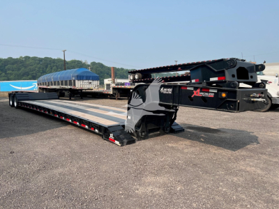 XL Specialized XL80HD trailer in lowboy configuration with extended deck and gooseneck, black frame, blue tarps in background, equipment on site.