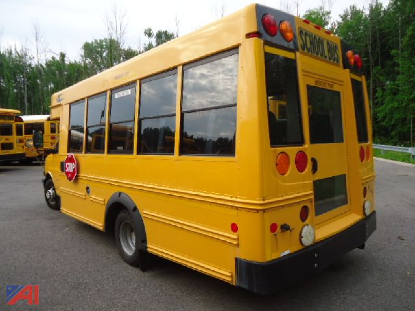 Yellow Chevrolet Express school bus viewed from rear-left angle with 'SCHOOL BUS' sign at rear and stop sign on side.