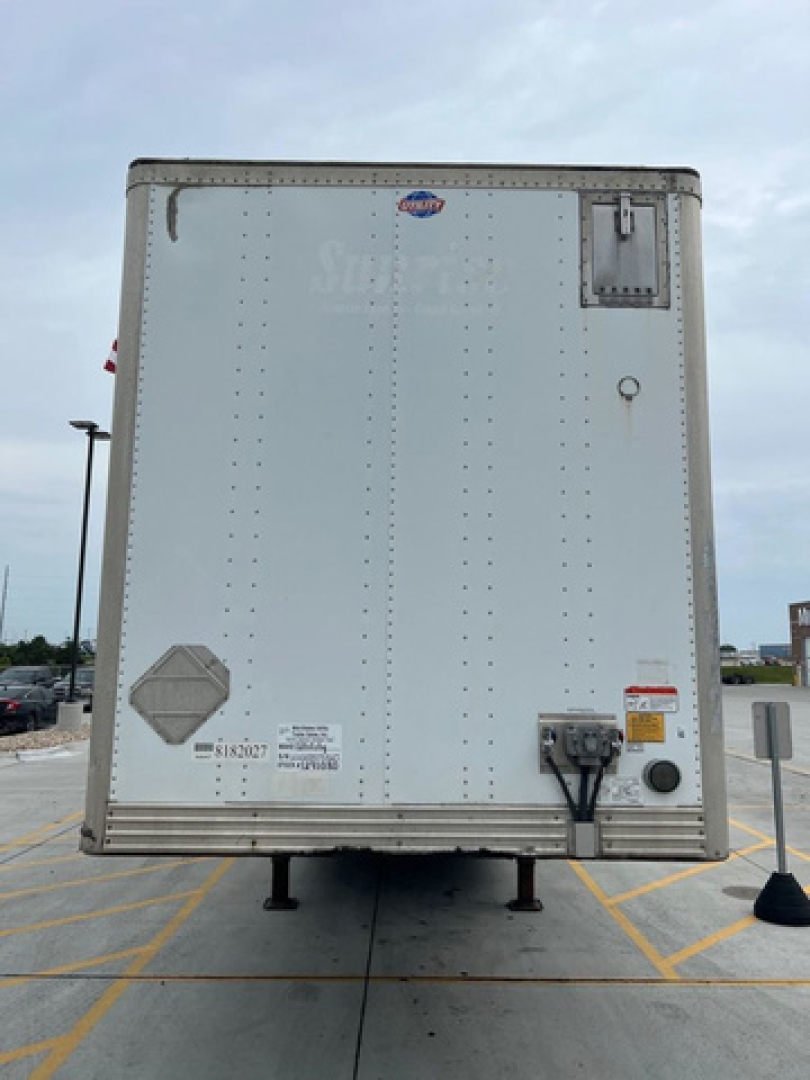 Rear view of a white cargo trailer showing landing gear legs, rear doors, reflectors, and small stickers.