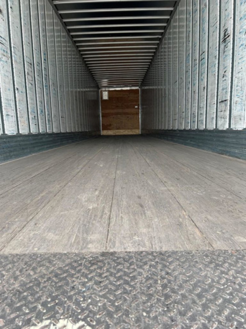 Trailer interior showing empty cargo space with metal side walls and wooden bulkhead at far end.