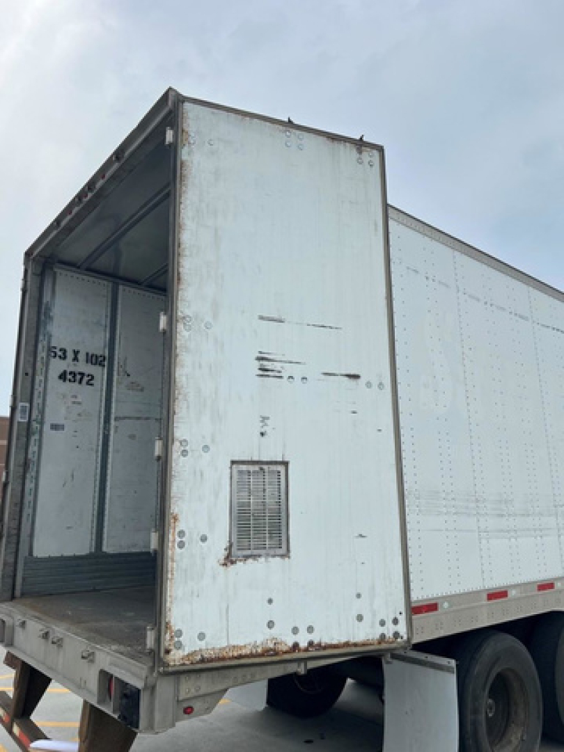Trailer rear doorway open showing interior of a utility van trailer with light blue doors and rust spots.