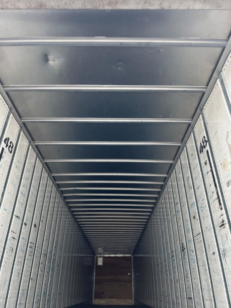 Trailer interior with metal walls and ceiling ribs; numbers 418 and 459 stamped on side panels; view toward rear with wooden floor at end.