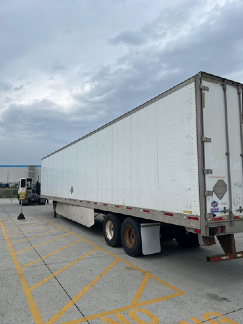Utility van trailer side and rear showing aluminum exterior, dual rear axles, and rear doors.