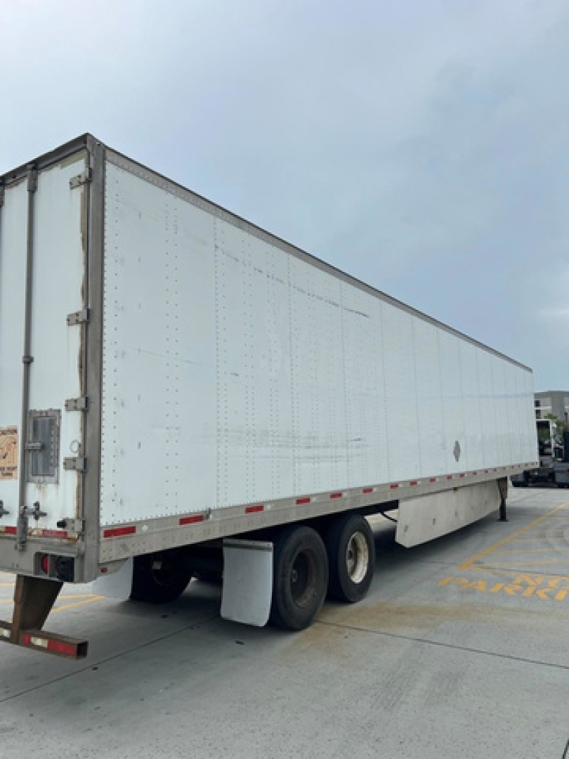 Utility van trailer showing side and rear with white riveted panels and triple-axle configuration.