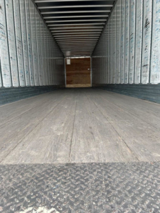 Trailer interior showing empty cargo space with metal side walls and wooden bulkhead at far end.