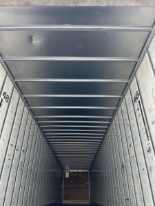 Trailer interior with metal walls and ceiling ribs; numbers 418 and 459 stamped on side panels; view toward rear with wooden floor at end.