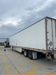 Utility van trailer side and rear showing aluminum exterior, dual rear axles, and rear doors.