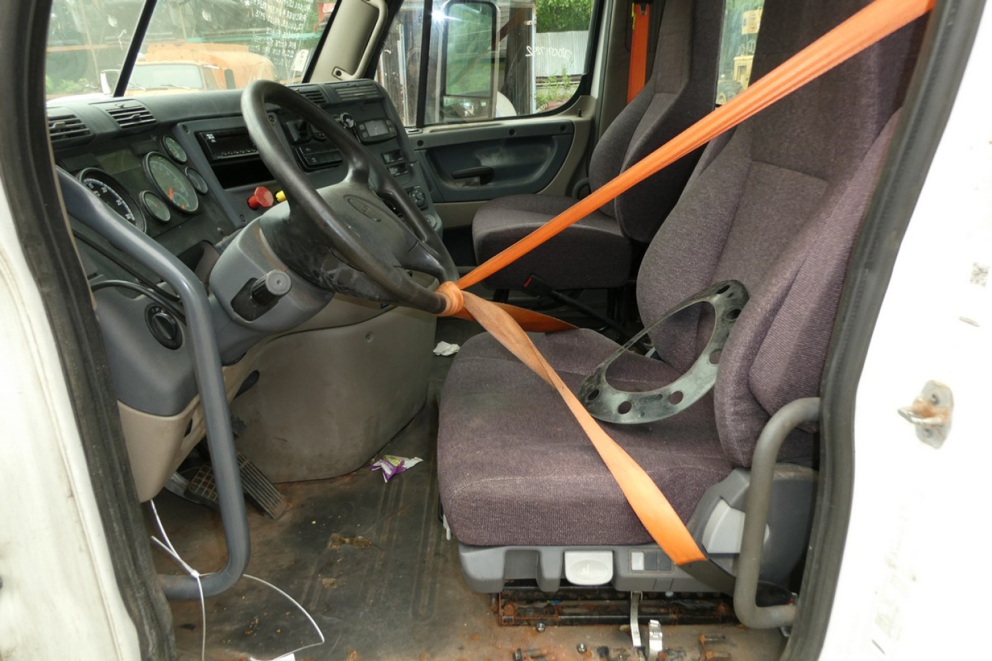 Freightliner Cascadia 125 truck interior cab view showing steering wheel, dashboard, and orange seatbelt across driver's seat.