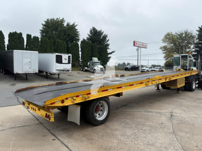 Landoll 330D-1 trailer in yard with long flatbed and gooseneck, showing front hitch and rear dual axles; yellow trailer with black deck, surrounding equipment in background.