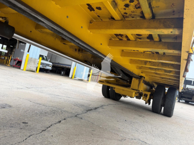 Underneath a yellow Landoll trailer showing structural beams and dual rear axles with tires, low-angle view.