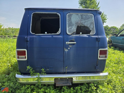 GMC Vandura full-size cargo van rear view showing broken rear windshield and side window, blue paint, chrome bumper.