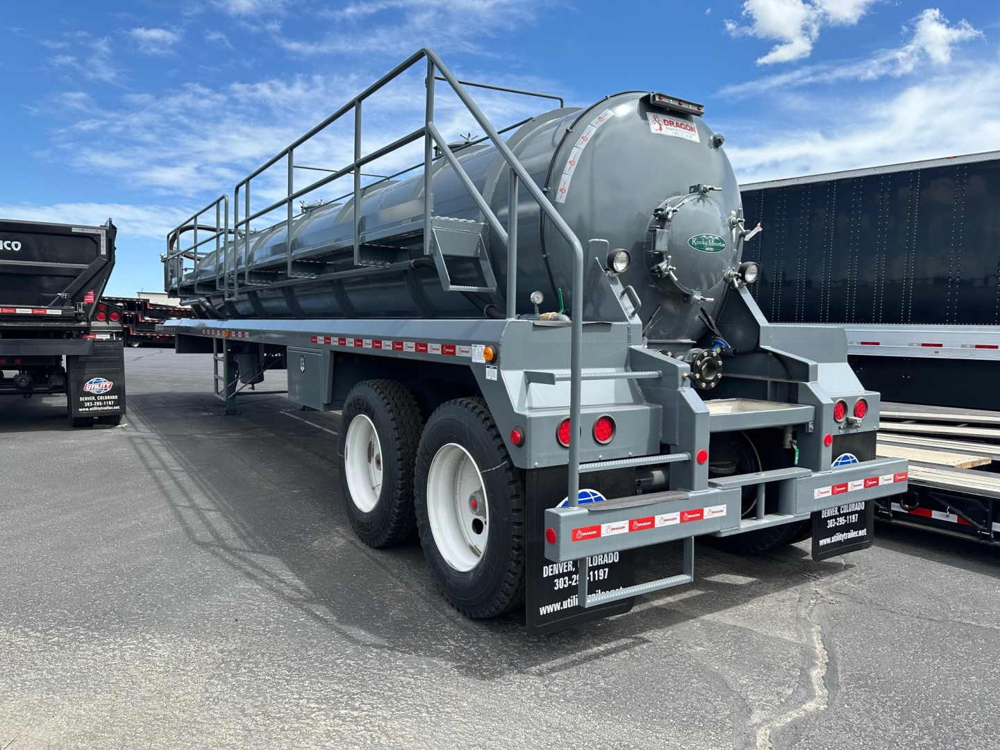 Trailer-mounted vacuum tank labeled Dragon Vac Tank with cylindrical tank on dual rear axles, ladder railing, rear lights, and gravel lot.