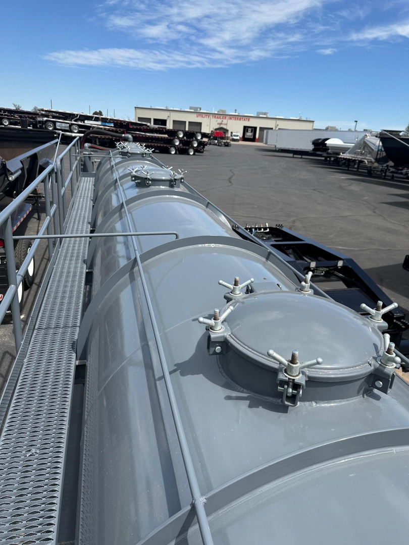Trailer vacuum tank on a dragon vac tank unit, long cylindrical tank with manhole access and clamps, outdoor lot with other trailers in background.