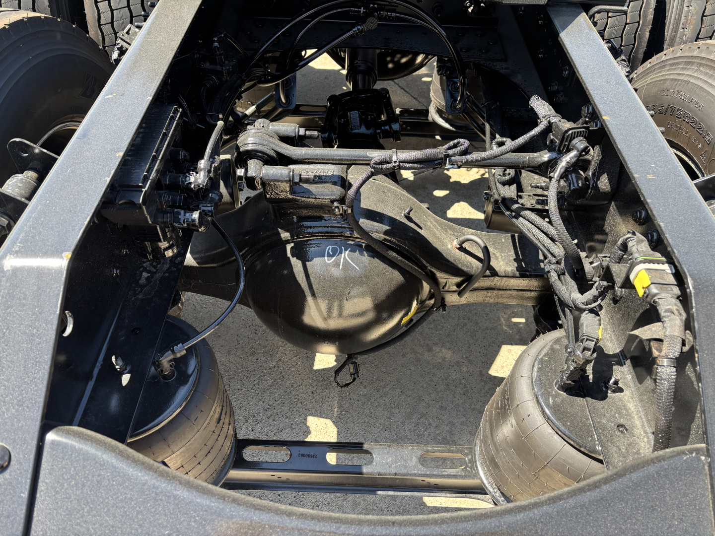 Truck chassis underside view showing differential, suspension, and various hoses and wiring in the drive area.
