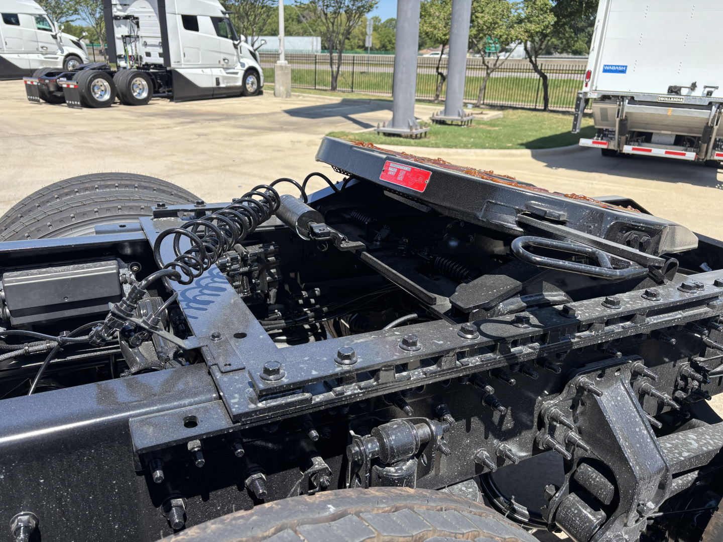 Volvo VNL cabless chassis view showing frame rails, fifth wheel area, and wiring harness on truck yard.