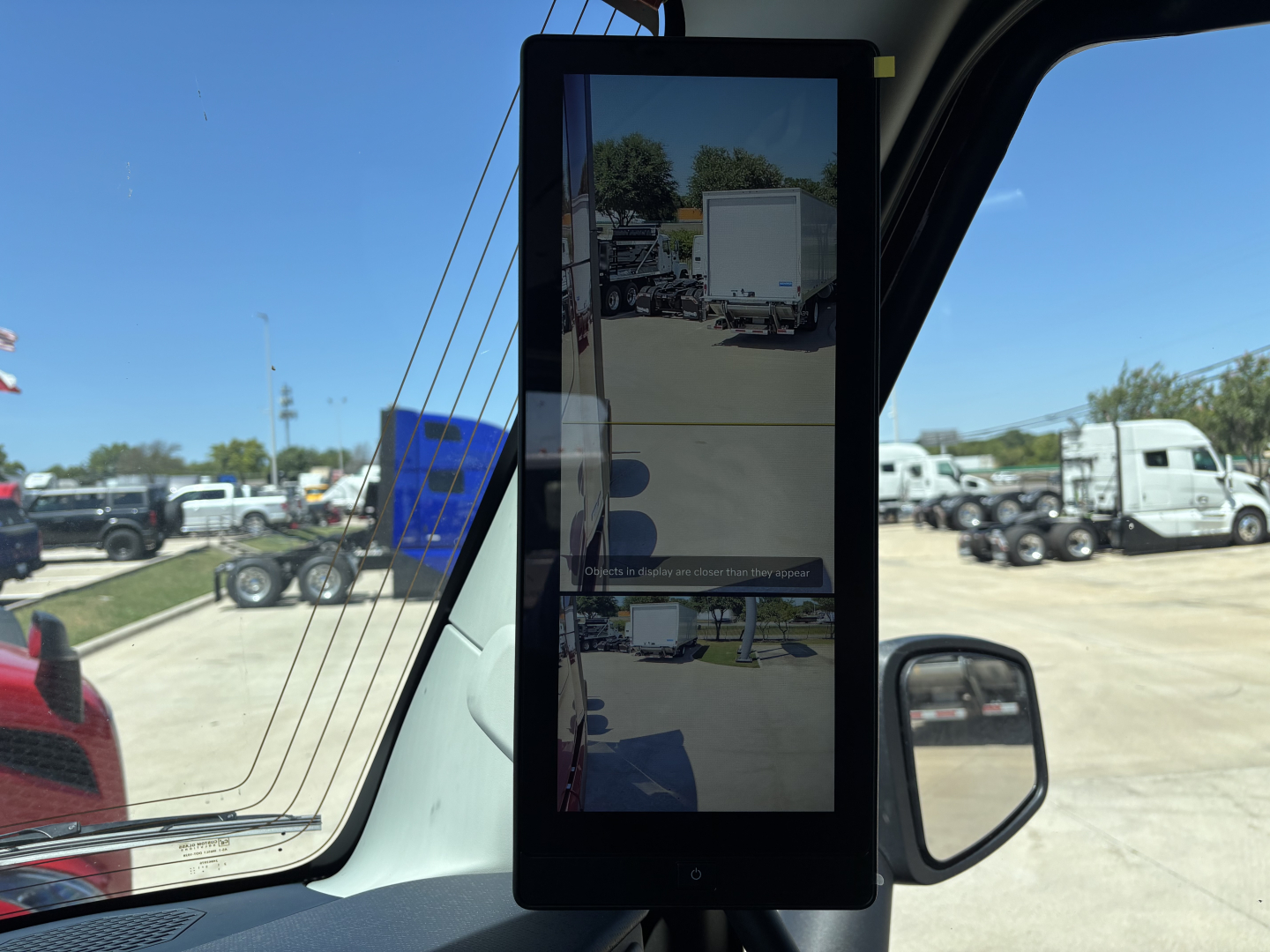Dashboard tablet mounted in Volvo VNL64T860 cab showing side mirror, interior window and reflection of a truck yard.