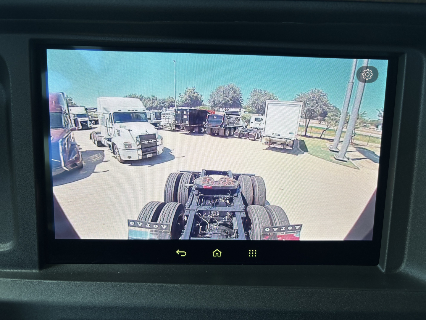 View from interior camera showing rear tractor axles and surrounding trucks in a dealership lot.
